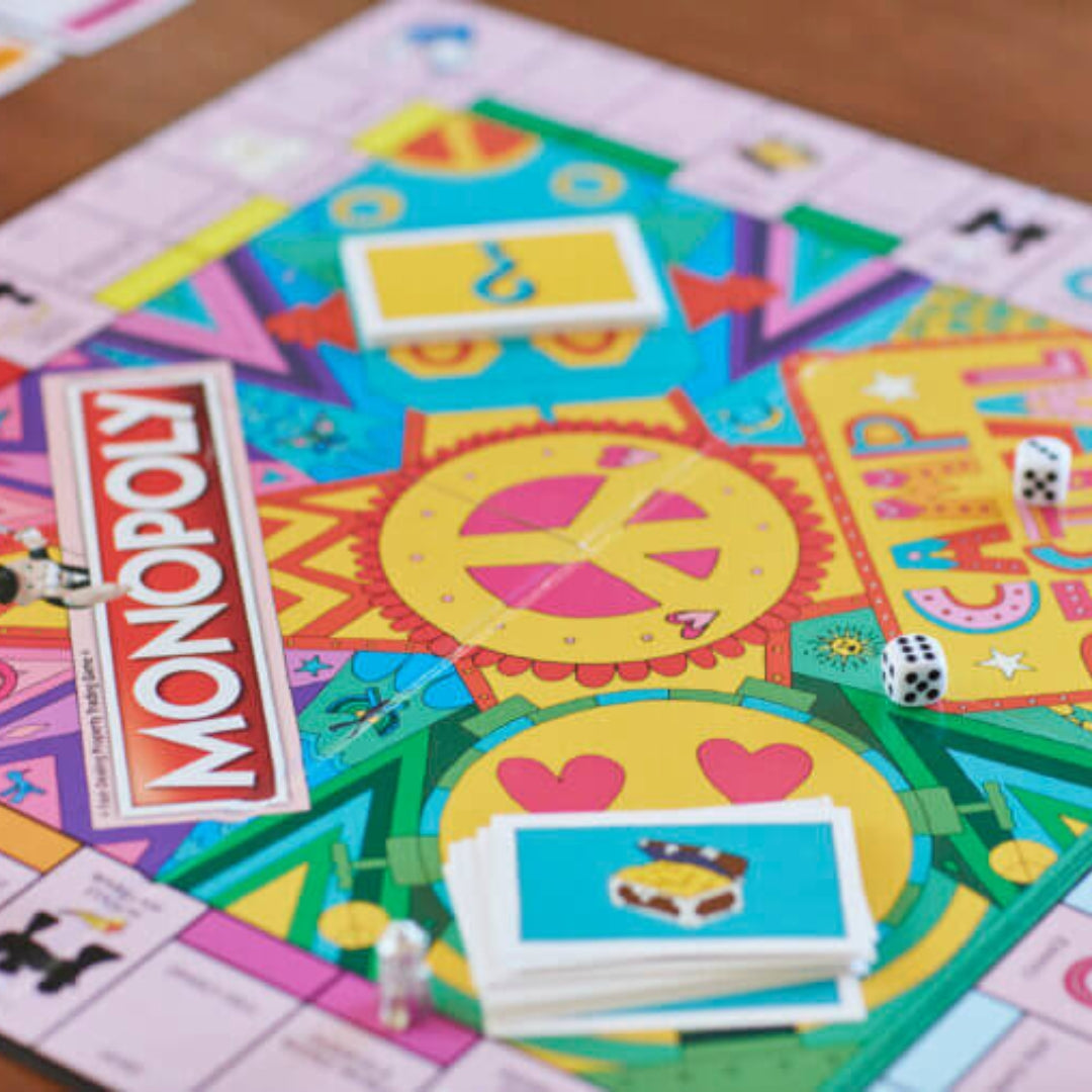 A close-up of the vibrant Camp Bestival Monopoly board by Camp Bestival, featuring a peace sign, dice, cards, and pieces—this limited-edition game captures the festival magic with its lively Camp theme.