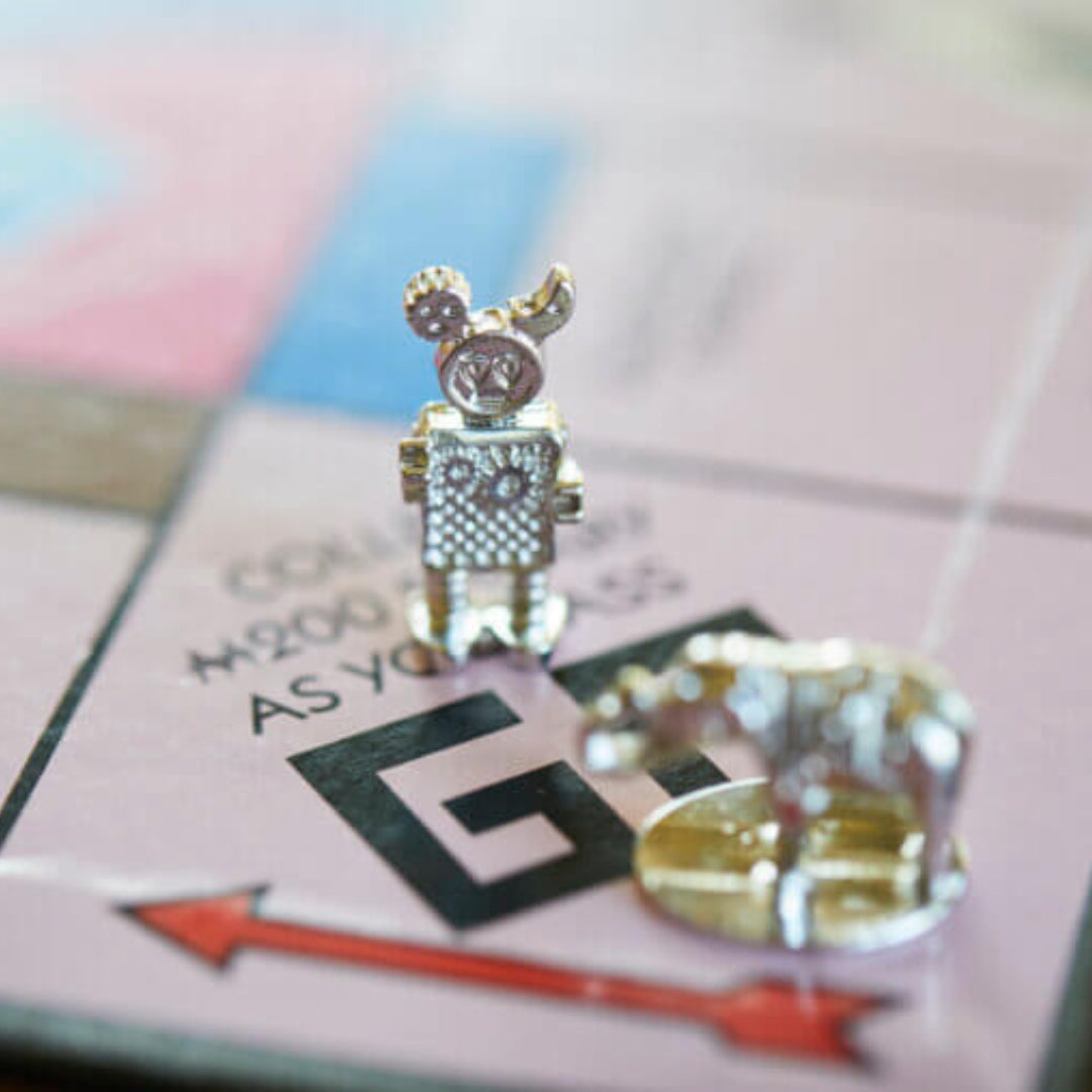 A close-up of two silver tokens, a robot and a dog, on the GO space of the Camp Bestival Monopoly board by Camp Bestival. The unique festival-inspired details of this limited-edition game and its tokens are shown in sharp focus.