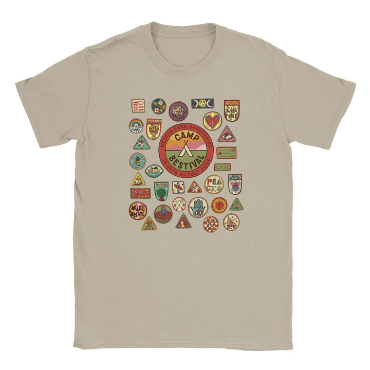 The Camp Bestival 2024 Shropshire Event T-Shirt by Camp Bestival is a beige, preshrunk ringspun cotton tee with a large central event badge, colorful camp-style patches, and a seamless double-needle collar for comfort.
