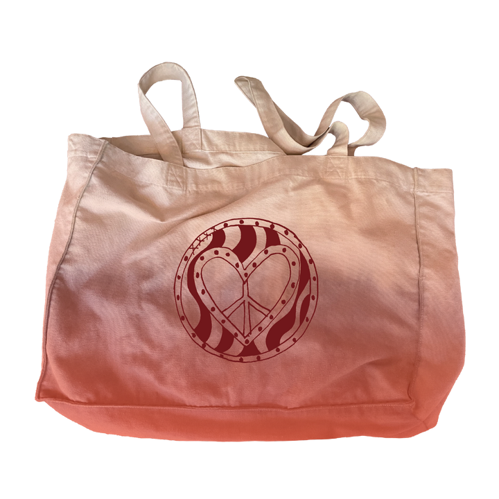 The Camp Bestival Family Tote Bag by 2025 is a pink and white tote with handles, showcasing a red heart-shaped peace sign inside a wavy circular pattern on the front.